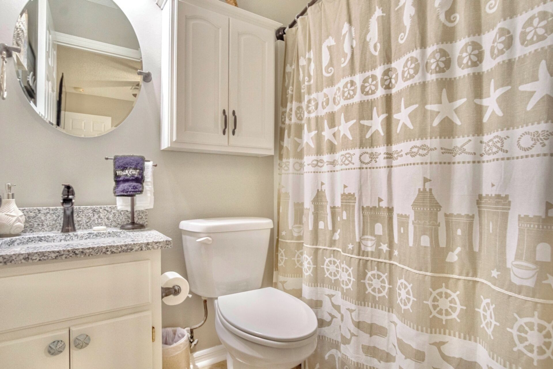 Une salle de bain comprenant des toilettes, un lavabo avec un miroir et un rideau de douche orné de motifs marins.