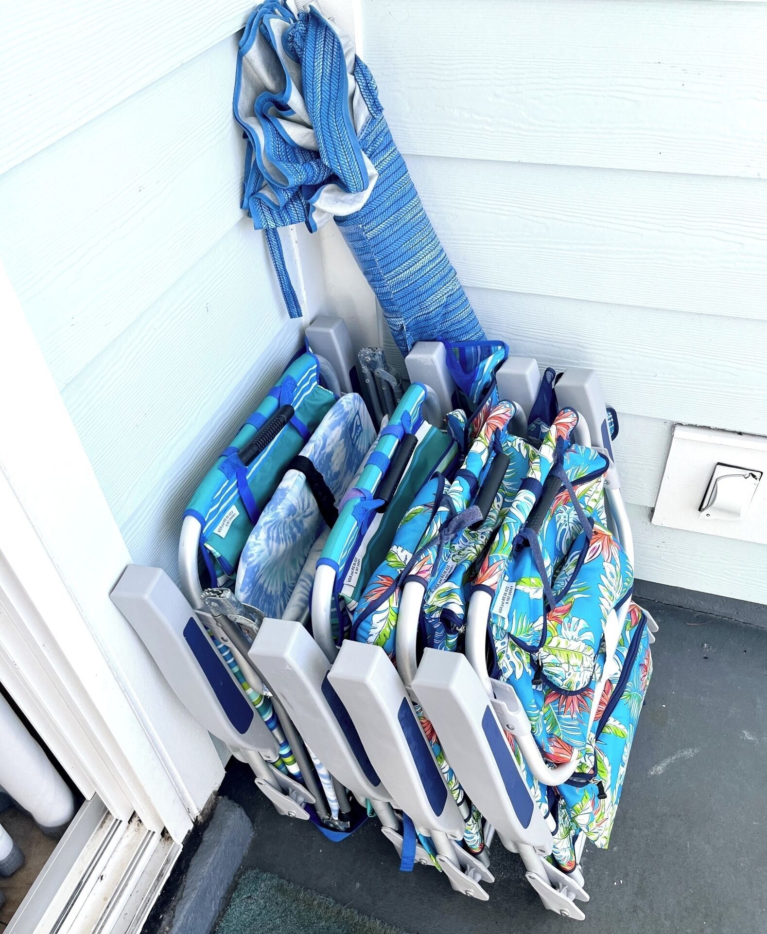 Un ensemble de chaises longues dotées de coussins bleus et blancs, une serviette bleue et un sac coloré appuyés contre un mur blanc.