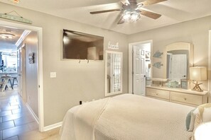 A bedroom with a bed, a ceiling fan, a dresser, a mirror, and a door leading to another room. - 🏖️ Coastal Family Escape - Sandy Seahorse Condo near Seaside w/ Pools & Tram (Santa Rosa Beach)