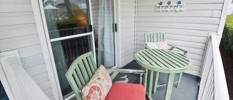 A covered porch with a green chair and table, a sliding glass door, and a small outdoor area with a doormat.