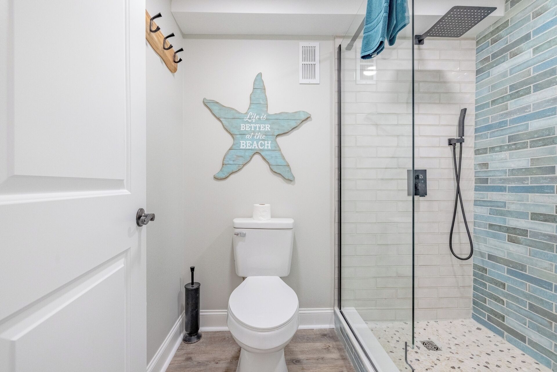 Un baño con inodoro blanco, un letrero con forma de estrella, cabina de ducha de vidrio y una toalla azul colgada en la puerta del box.