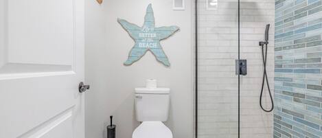 Un baño con inodoro blanco, un letrero con forma de estrella, cabina de ducha de vidrio y una toalla azul colgada en la puerta del box.