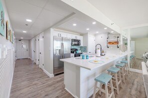 A modern kitchen with a central island, bar stools, and a microwave. - Sandy Sunsets Tower 3 - 6th floor, gorgeously updated beachfront w/2 king beds+ (Panama City Beach)
