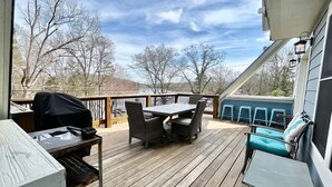 Un patio in legno con mobili da esterno, un barbecue e vista su alberi e colline.
