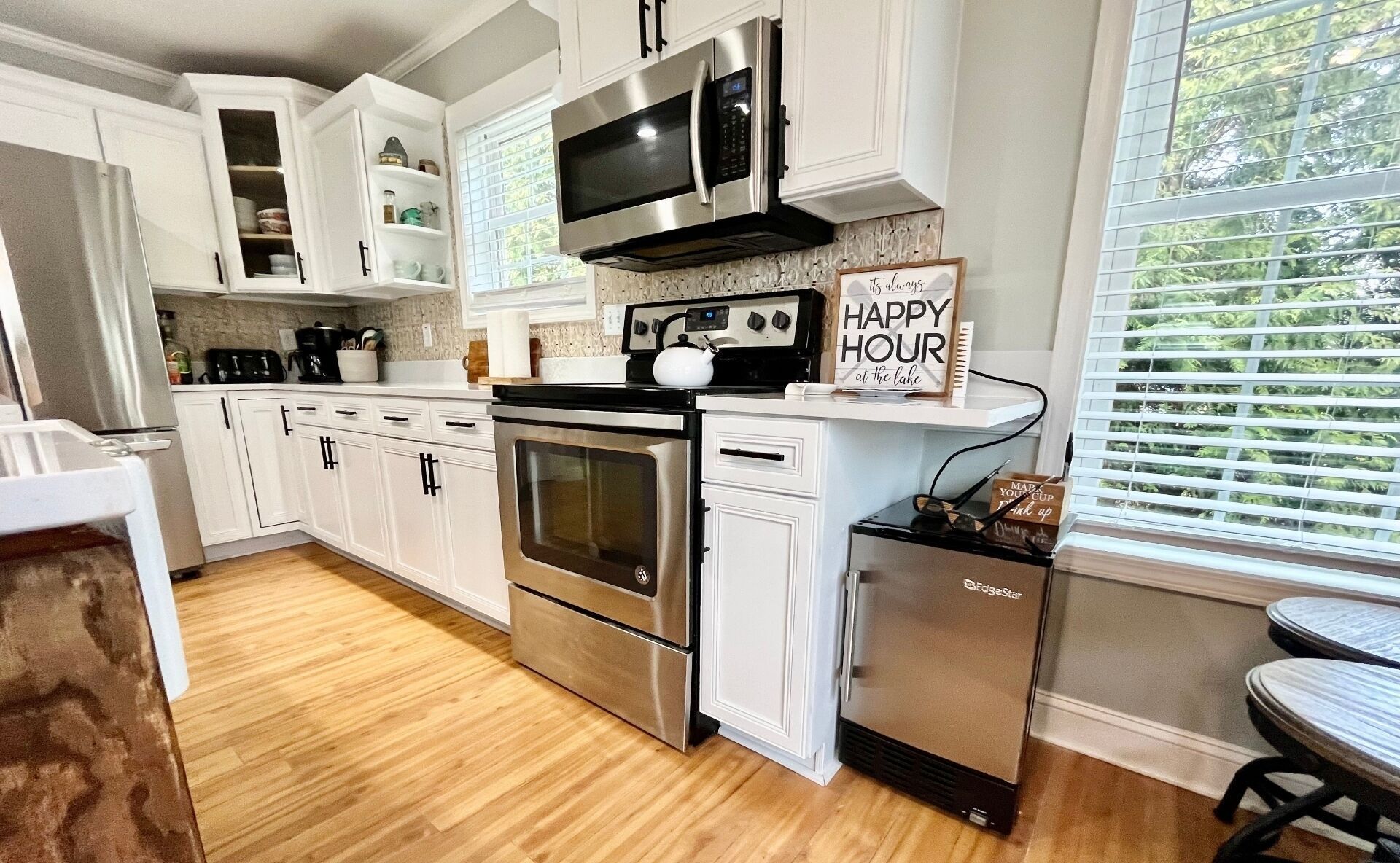 A modern kitchen with stainless steel appliances, white cabinetry, and a view of the outdoors through large windows.