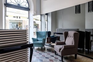 A modern interior with a large window, two armchairs, a small table, and a patterned floor.