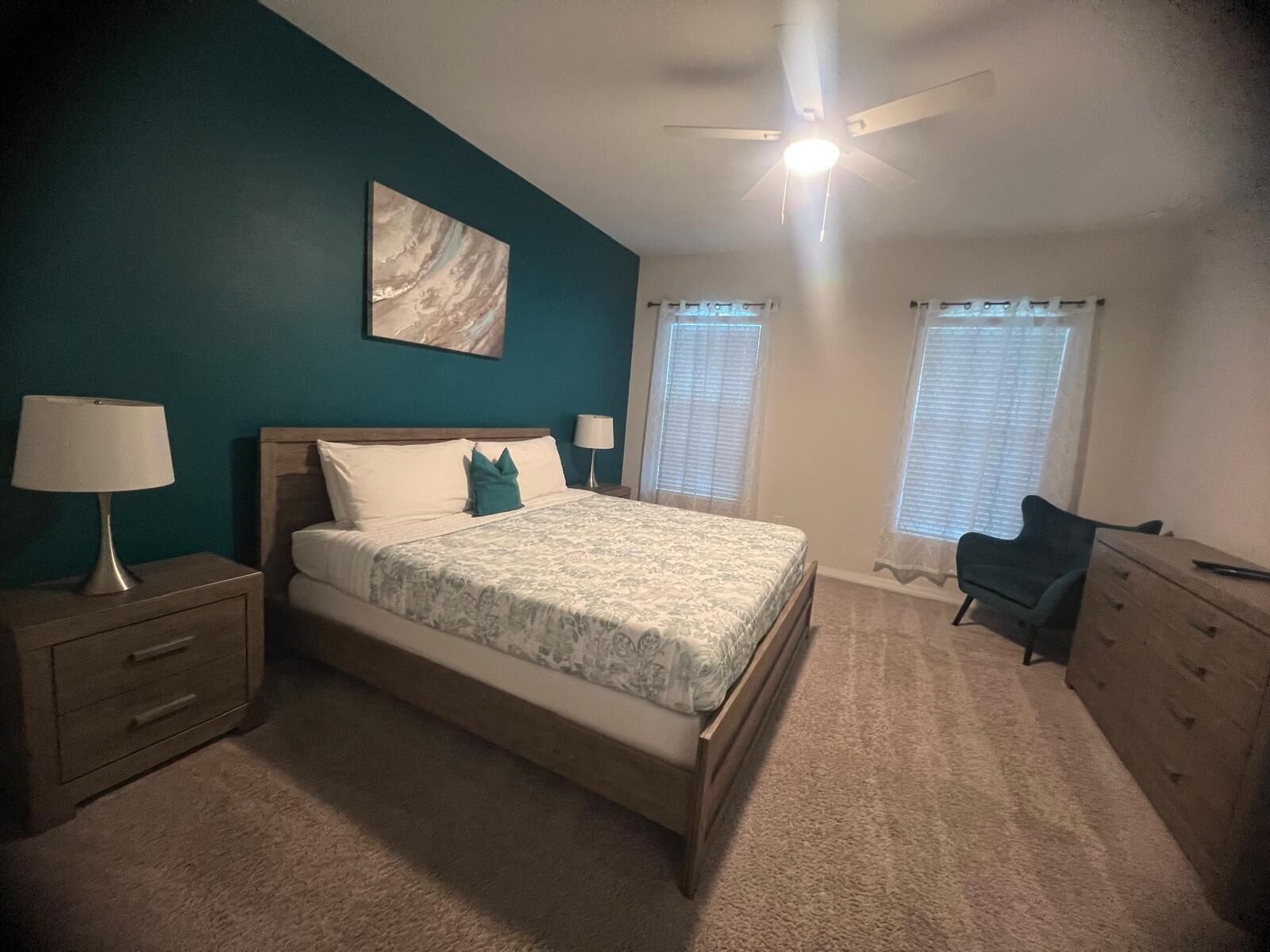 A bedroom with a bed, nightstands, a dresser, a ceiling fan, and a window with blinds.