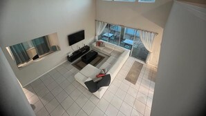 Uma sala de estar moderna com uma televisão de tela plana, um sofá, uma mesa de centro e um espaço de jantar com mesas e cadeiras.