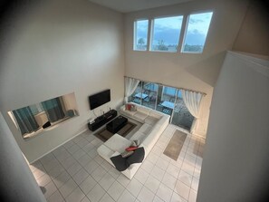 Ein modernes Wohnzimmer mit Flachbildfernseher, einer Couch, einem Couchtisch und einem Essbereich mit Tischen und Stühlen.