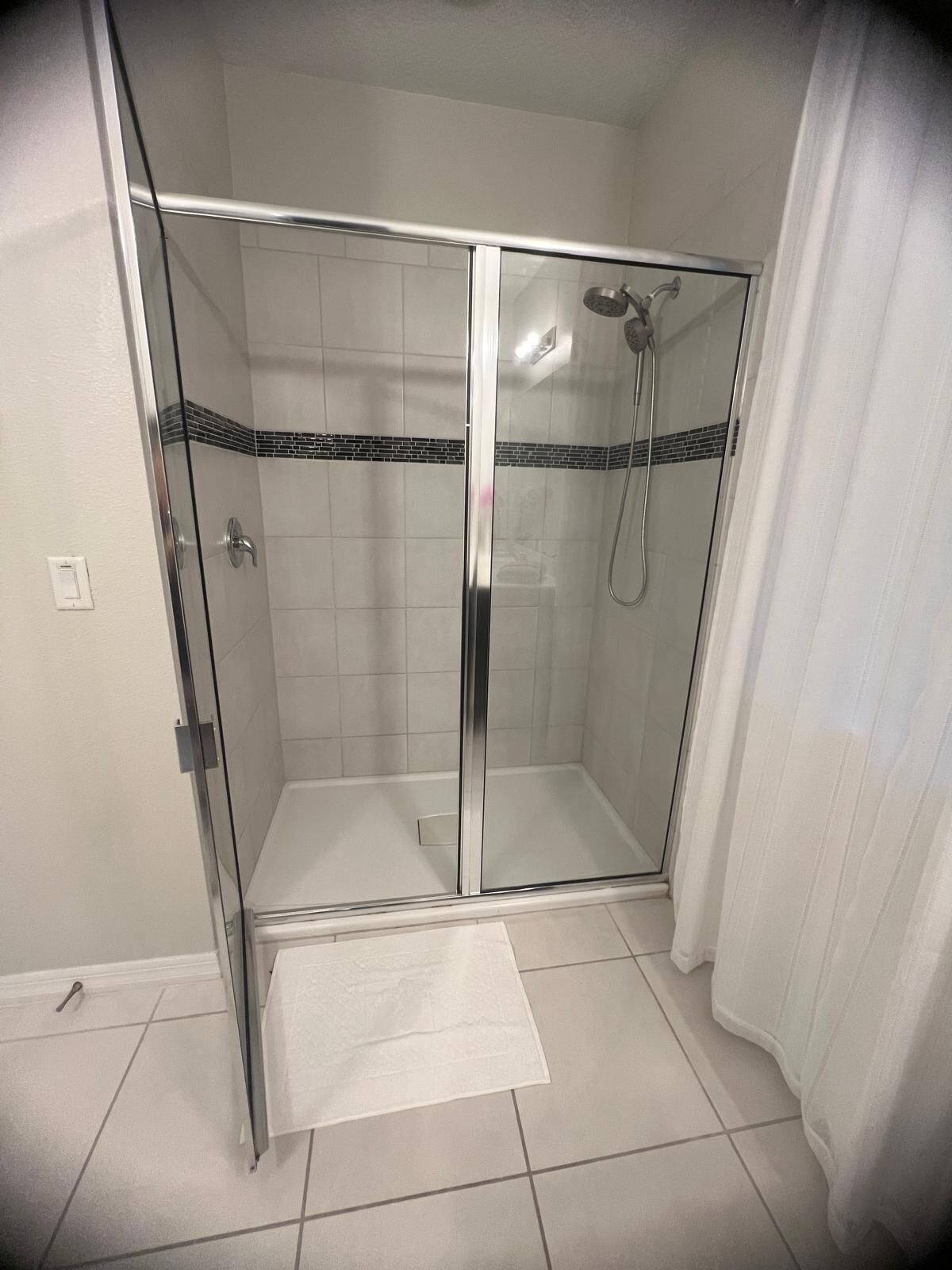 A glass-enclosed shower stall with a showerhead and handheld shower attachment.
