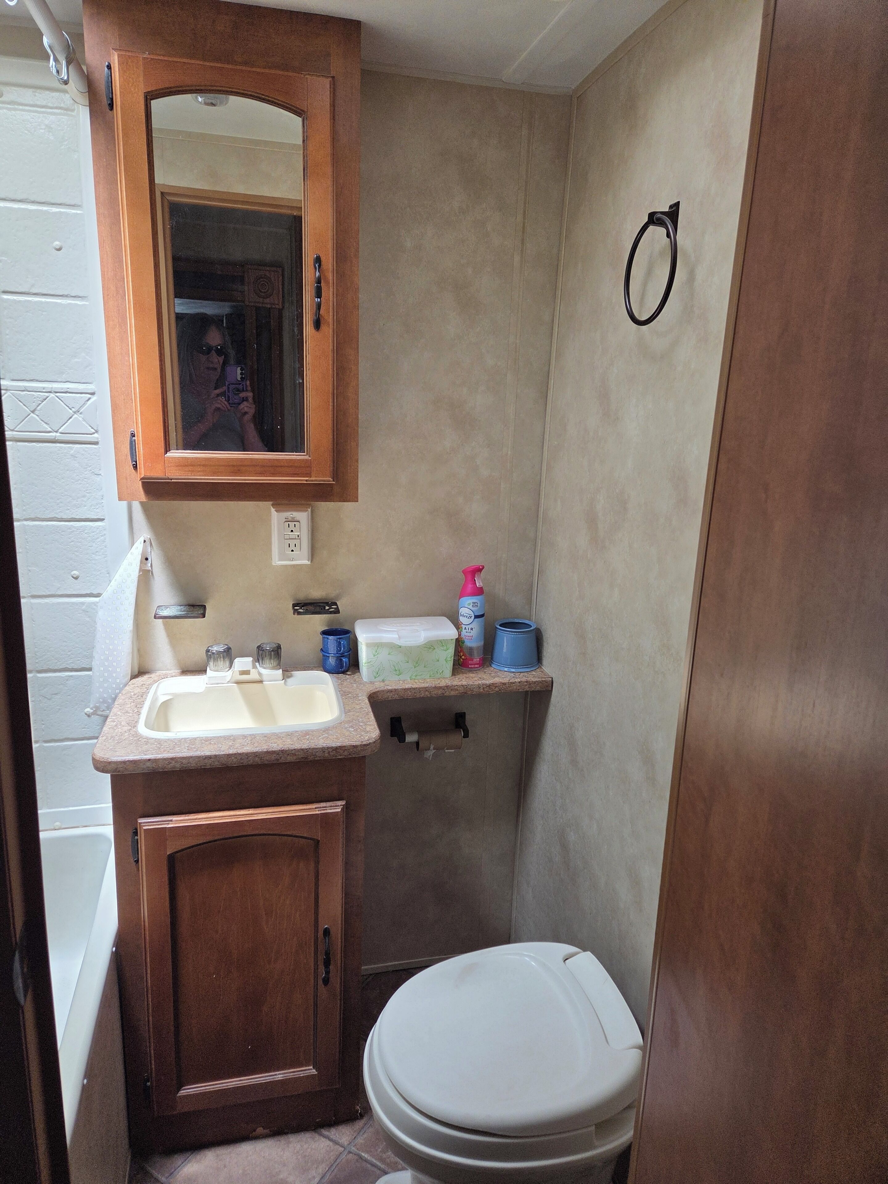 A compact bathroom with a wooden vanity, a sink, a toilet, and a mirror.