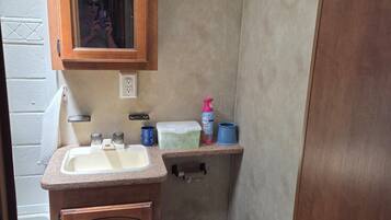 A compact bathroom with a wooden vanity, a sink, a toilet, and a mirror.
