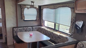 A cozy RV interior with a dining area, seating, and a window with blinds.