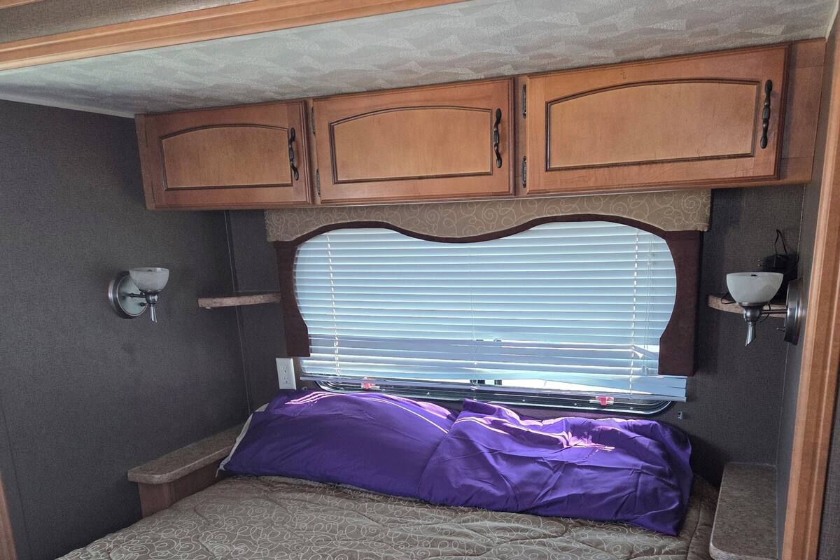 Un dormitorio con cama, cabecera, armarios y una ventana con persianas.