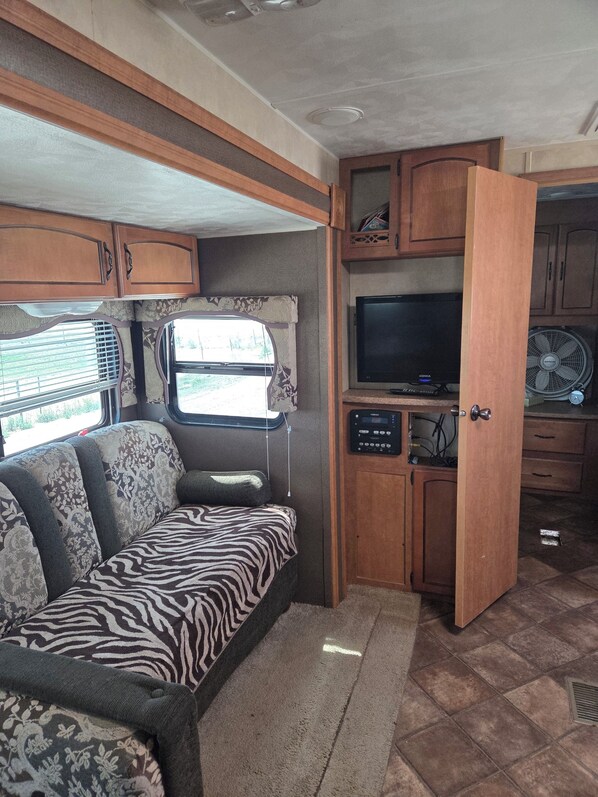 A compact RV interior with a sofa, a television, and a kitchenette area.