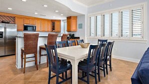 Une cuisine moderne avec des meubles en bois, un réfrigérateur en acier inoxydable et un coin repas comprenant une table blanche et des chaises bleues.
