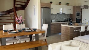 A modern kitchen with a built-in island, stainless steel appliances, and a dining area with a wooden table and chairs. - Seaview Villa Lagonissi |7-min Walk to Beach| Pool & SunsetViews |Athens Riviera (Kalivia Thorikou)