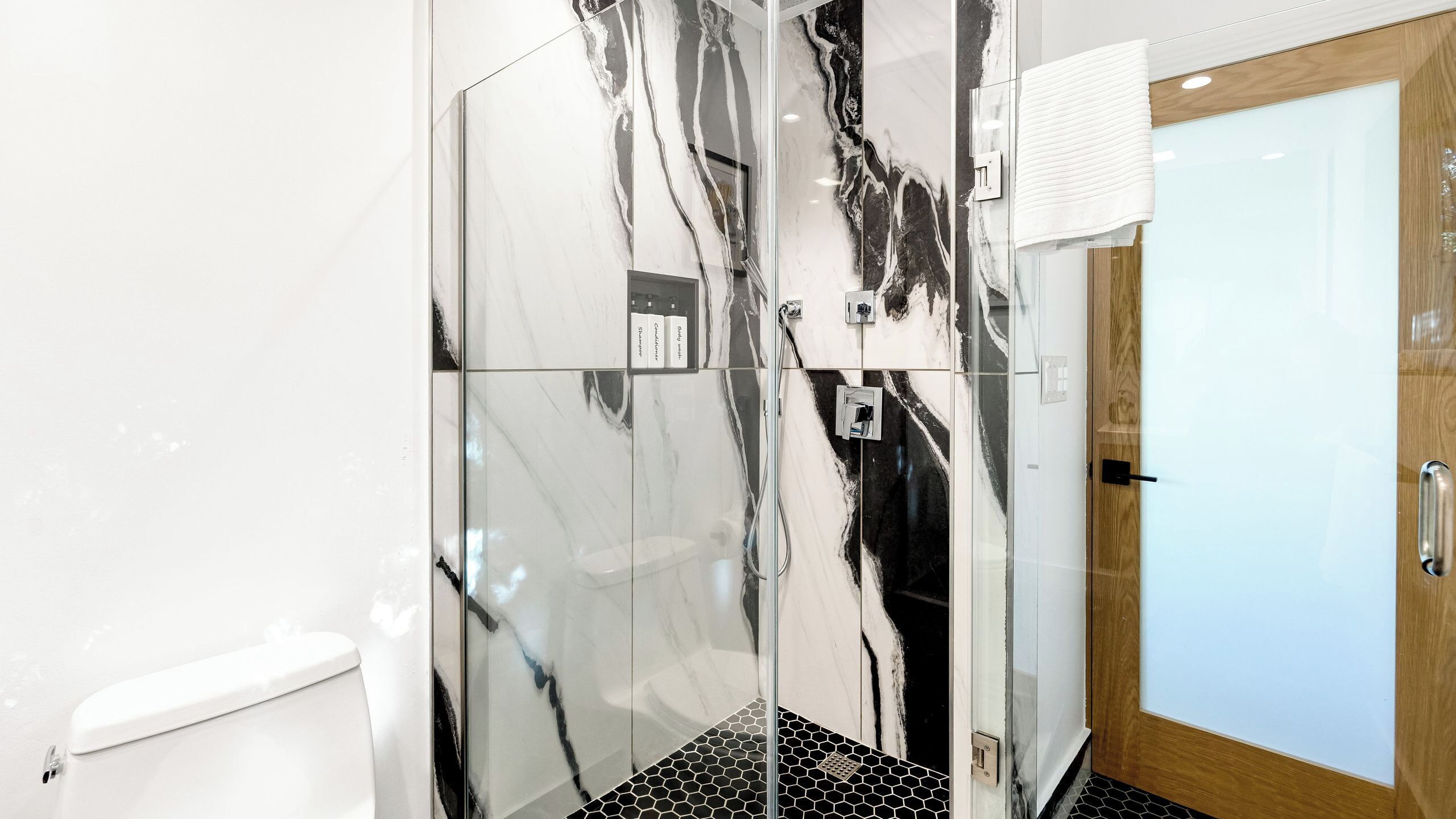 A bathroom with a glass shower enclosure, a toilet, and a wooden door.