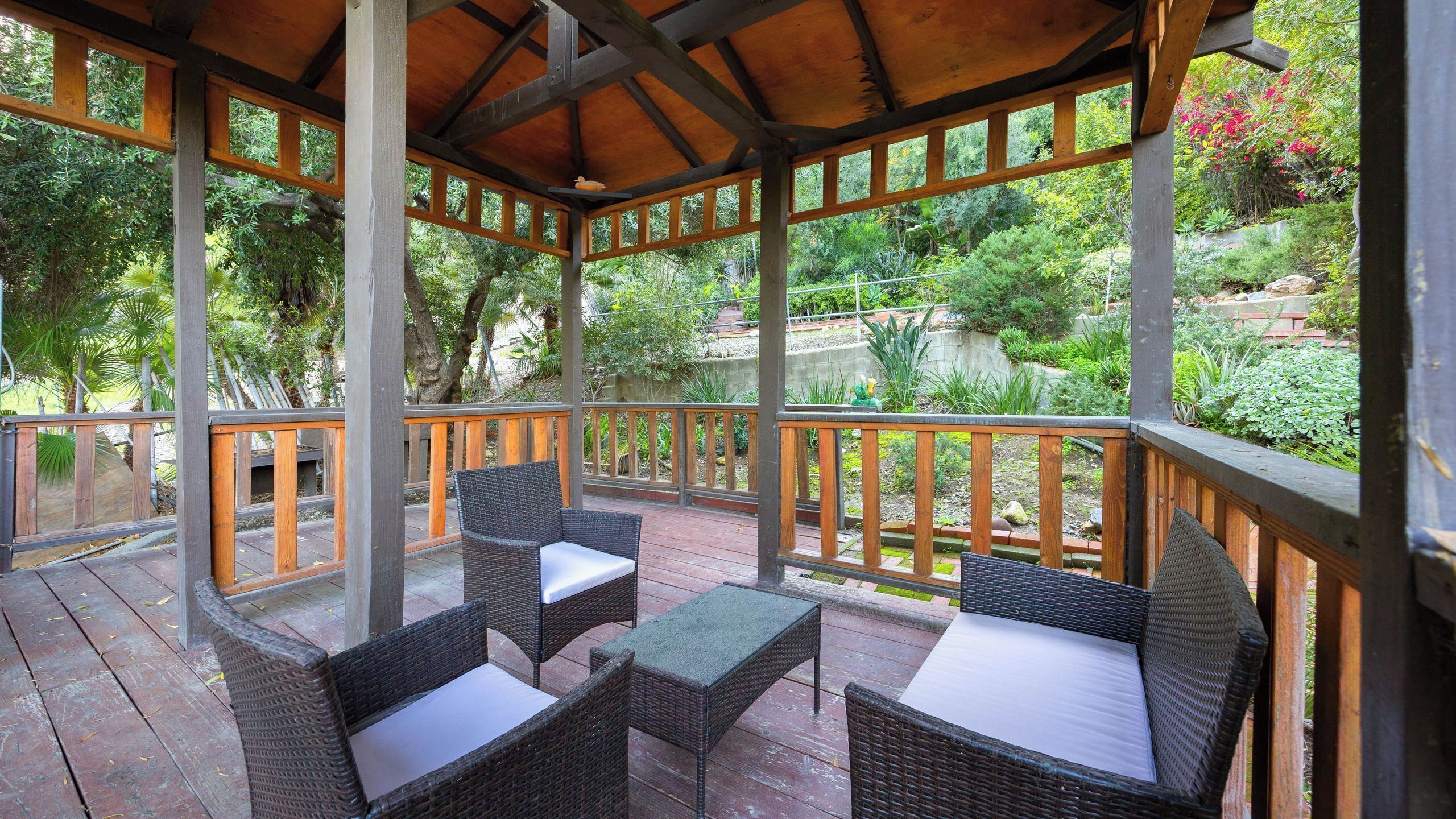 A covered outdoor seating area with wicker furniture and a view of lush greenery.