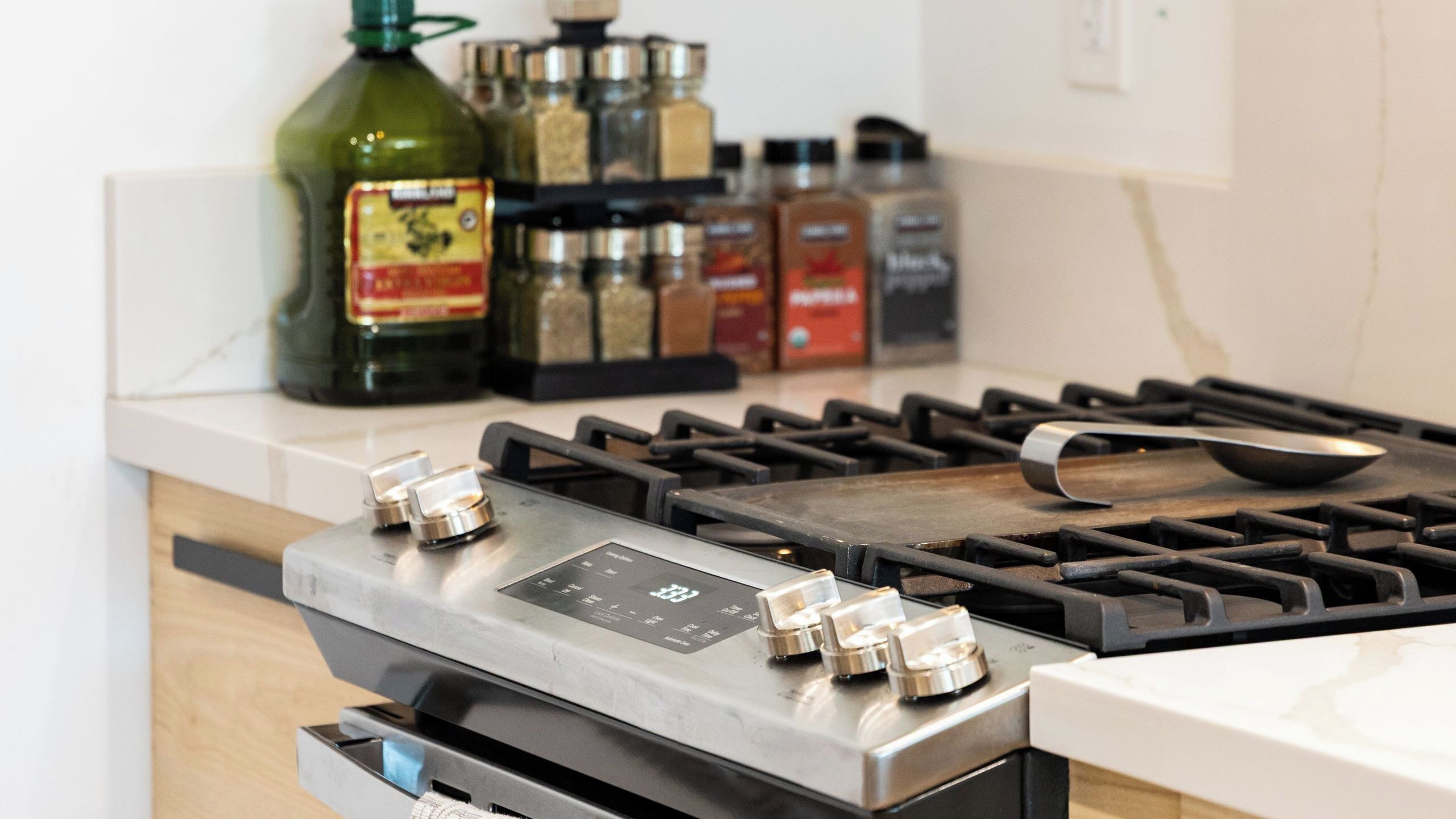 A kitchen with a gas stove, a digital control panel, and various condiments on the counter.