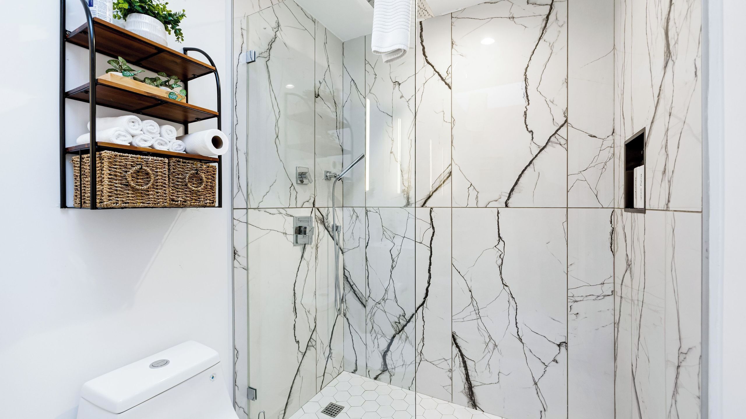 A bathroom with a shower, marble walls, a towel rack, and a soap dispenser.