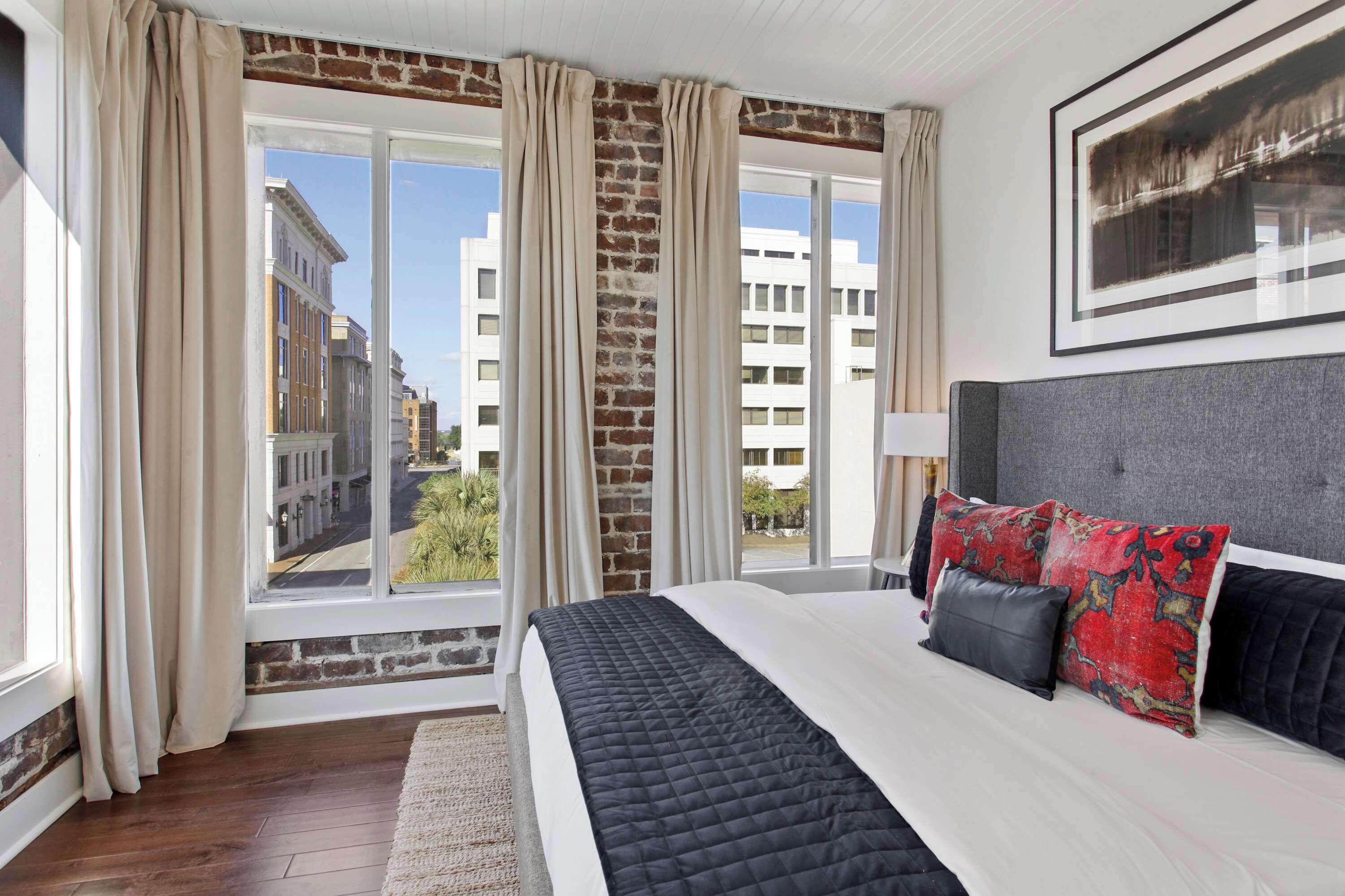 A bedroom with a large bed, a view of buildings, and a brick wall.