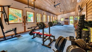 A gym with various exercise equipment, large windows, and a wooden ceiling.