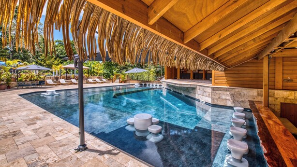 A swimming pool with a wooden deck, lounge chairs, and a thatched roof structure.
