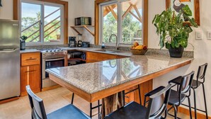 A modern kitchen with a large island, bar stools, a ceiling fan, pendant lights, and a view of the outdoors.