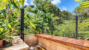 A stone bench with a wooden top, surrounded by lush greenery and a metal fence.