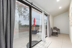 Habitación con puerta de vidrio corredera a un patio exterior, una silla blanca, una mesita y un paraguas rojo.