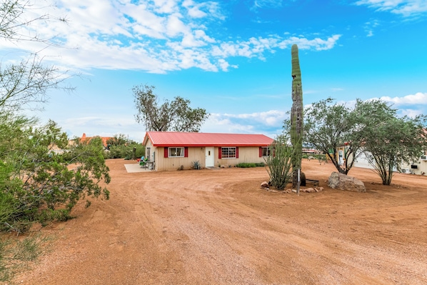 A single-story building with a red roof, a dirt driveway, and sparse vegetation.