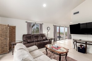 A modern living room with a leather sofa, a glass coffee table, a flat-screen TV, and a sliding glass door leading to an outdoor area.