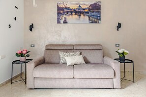 A beige sofa with a patterned pillow, two side tables with potted plants, and a wall-mounted picture of a bridge. - [luggage storage] - La Bellavita Trastevere (Roma)