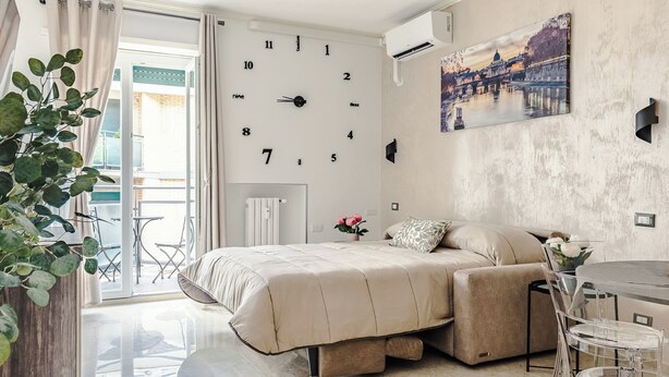 Ein Schlafzimmer mit einem Bett, einer Wanduhr, einem Fenster und einem Gemälde.