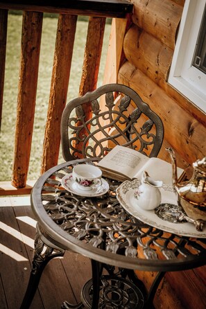 A wooden log cabin interior with a metal table set for tea, a book, and a teapot.
