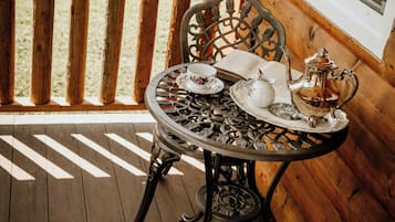 Um deck de madeira com uma mesa posta para um chá, uma cadeira e uma janela com mosquiteiro.