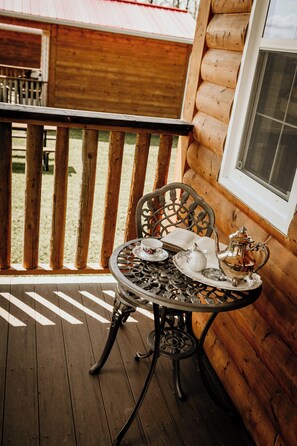 A wooden deck with a table set for tea, a chair, and a window with a screen.