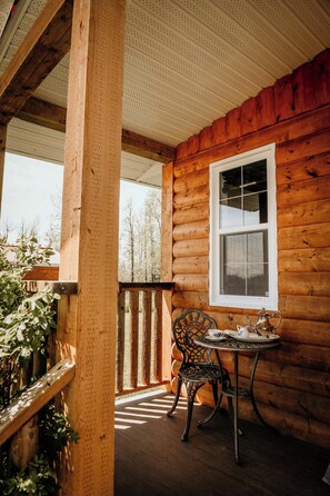 A wooden cabin with a porch, a table with chairs, and a window.
