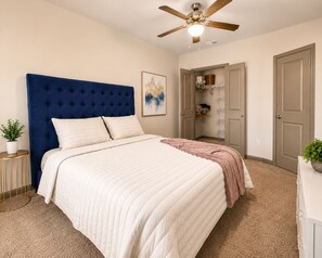 A bedroom with a tufted headboard, a bed with white bedding, a ceiling fan, a closet with shelves, and a door.