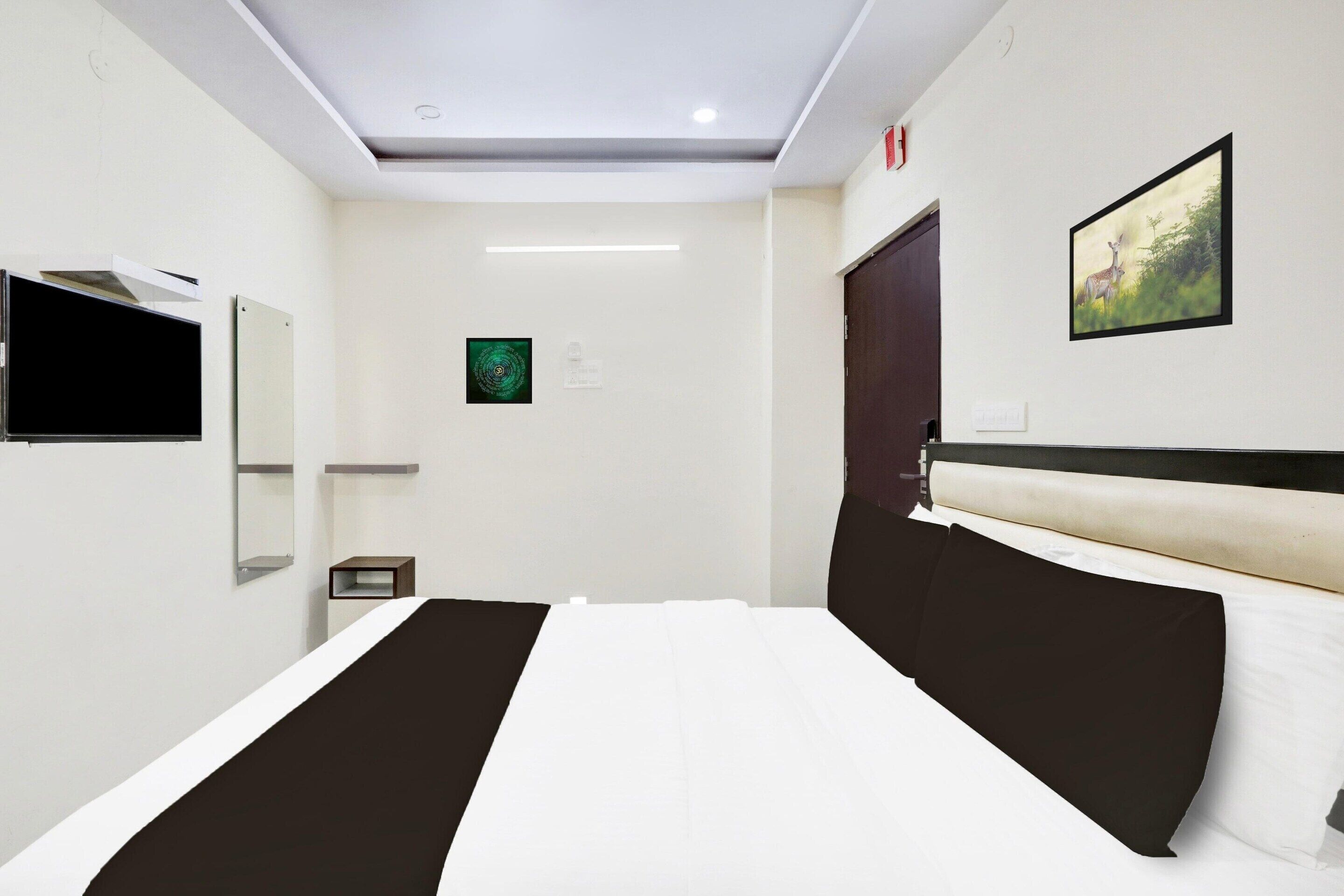 Une chambre d’hôtel avec un lit, un téléviseur à écran plat, un miroir, un tableau au mur et une porte.