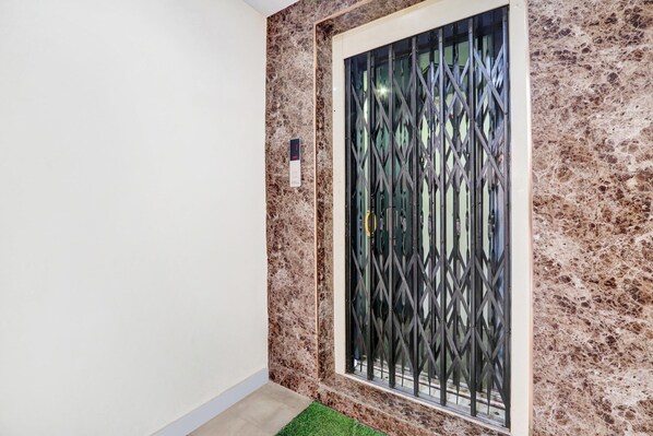 A hallway with a marble wall, a glass door with a metal security gate, and a small green area rug. - Deluxe With Twin Bed Lotus Park Hotel (Visakhapatnam)