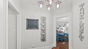 A hallway with a chalkboard sign, a wall clock, and a door leading to a dining area.