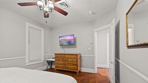 A bedroom with a bed, a dresser, a ceiling fan, a TV, and a door.