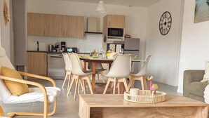 Un salon moderne avec une table basse en bois, des chaises blanches et un coin repas comprenant une table et des chaises en bois.