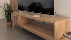 Un téléviseur à écran plat fixé sur un meuble télé en bois, avec une plante à côté.