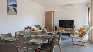 Un coin repas avec une table en bois dressée pour quatre personnes, un téléviseur et un espace salon comprenant un canapé et des fauteuils.