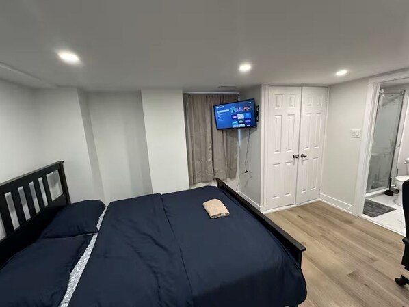 A bedroom with a bed, a TV mounted on the wall, a wardrobe, and a shower area.