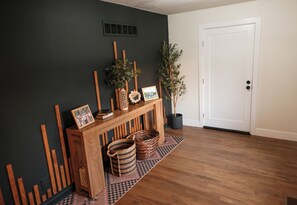 Une pièce avec un mur de couleur sombre, une console en bois agrémentée de paniers et d’une plante en pot, un tapis à motifs et une porte blanche.