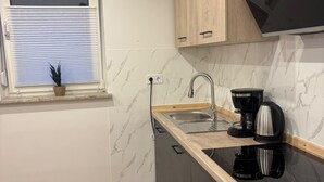 Moderni keittiö, jossa on sisäänrakennettu astianpesukone, pesuallas, kahvinkeitin ja puukehikoiset kaapit.